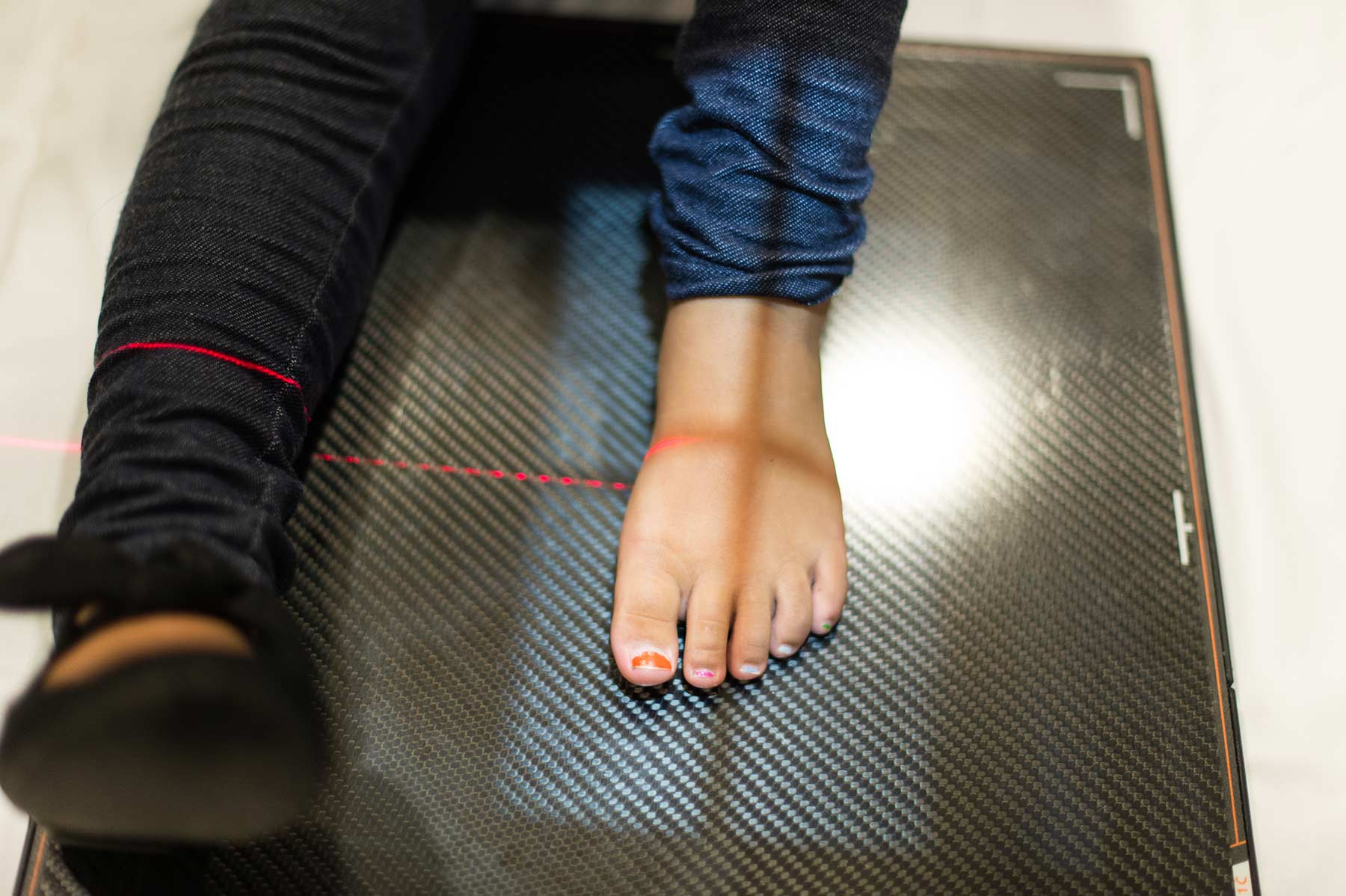 A child with a shoe on one foot and a bare foot sits on a table for a scan