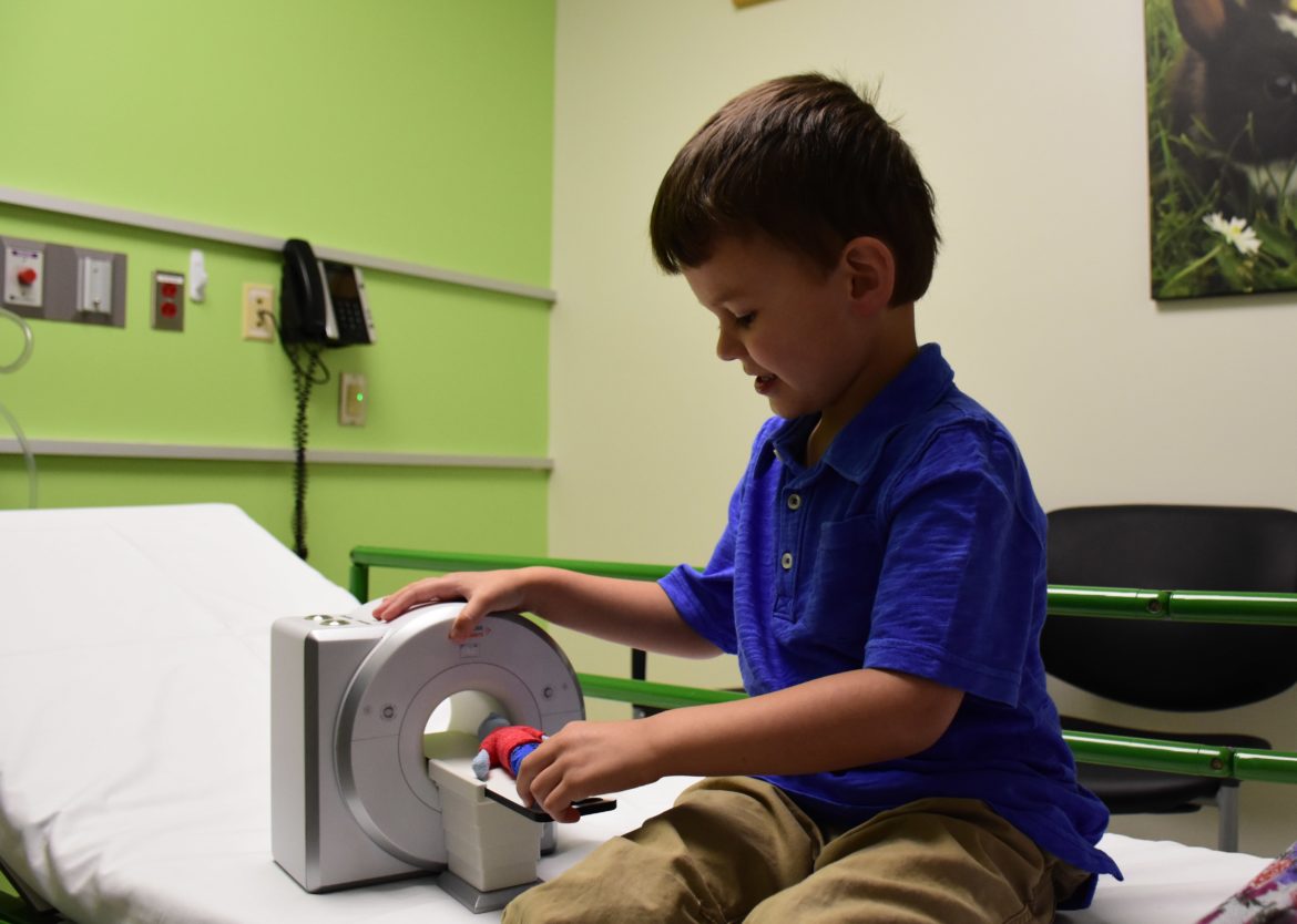 A boy sits in a waiting room playing with a toy man and MRI machine